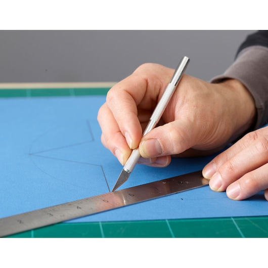 STANLEY 0-10-401 hobbymes snijdt blauw papier langs metalen liniaal, close-up fotografie.