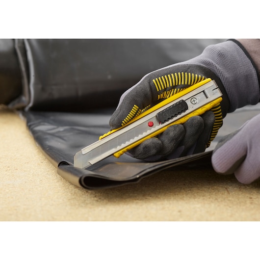 STANLEY 0-10-431 hobbymes snijdt zwart materiaal, close-up van een gehandschoende hand met het gereedschap.