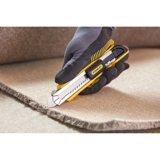 Stanley 0-10-481 hobbymes snijdt tapijt, geel-zwart gereedschap in hand.