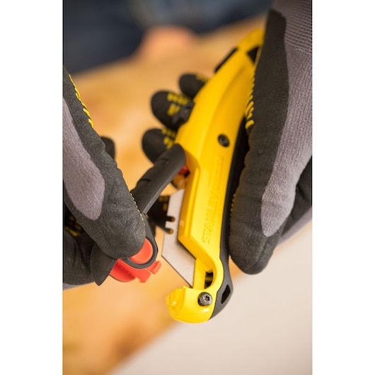 Photo du couteau utilitaire STANLEY 0-10-778 jaune et noir utilisé avec des gants.