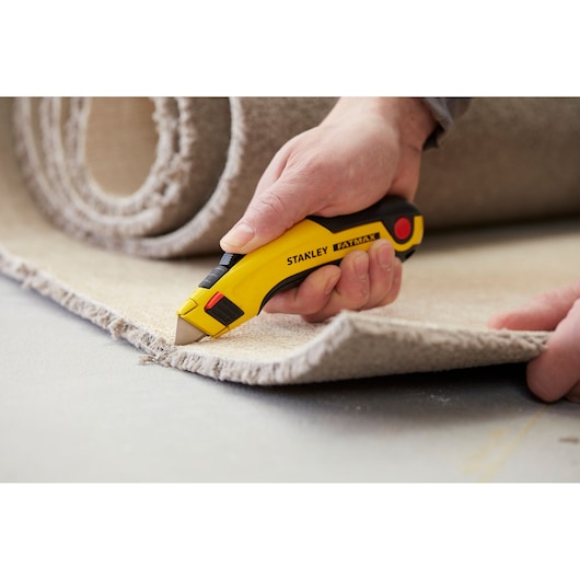 Couteau Stanley 0-10-778 coupant un tapis, photo en gros plan, manche jaune et noir, modèle FatMax.