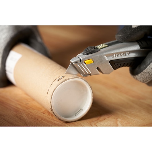 Photo du couteau utilitaire STANLEY 0-10-788 coupant un tube en carton sur une surface en bois, angle rapproché.