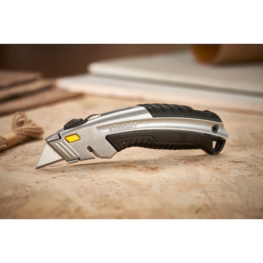 STANLEY 0-10-788 couteau utilitaire argenté et noir, posé en angle sur une surface de travail.
