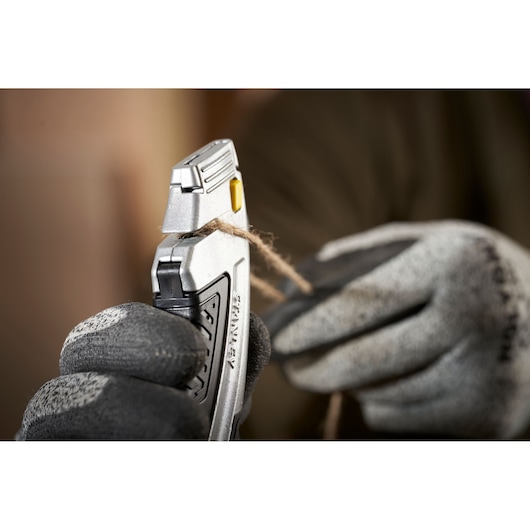 Photo du couteau utilitaire STANLEY 0-10-788 coupant de la ficelle, tenu avec des gants, gros plan.