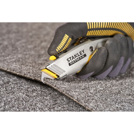 STANLEY 0-10-789 couteau utilitaire coupant un tapis, gros plan, manche gris et jaune.