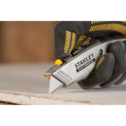 Stanley 0-10-789 couteau utilitaire utilisé pour couper du placoplâtre, photo en gros plan avec main gantée.