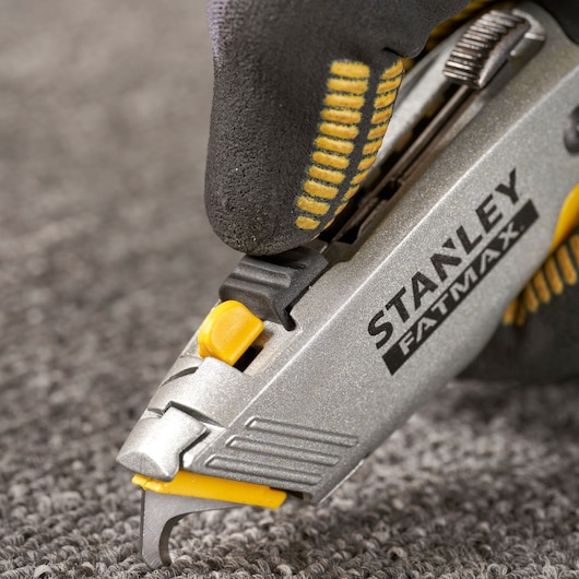 STANLEY 0-10-789 couteau utilitaire gros plan coupant tapis, poignée argent et jaune, main gantée.