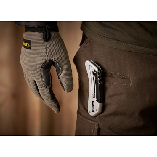 STANLEY 0-10-810 couteau utilitaire pliant accroché à une poche de pantalon marron, vue rapprochée de côté, main gantée proche.