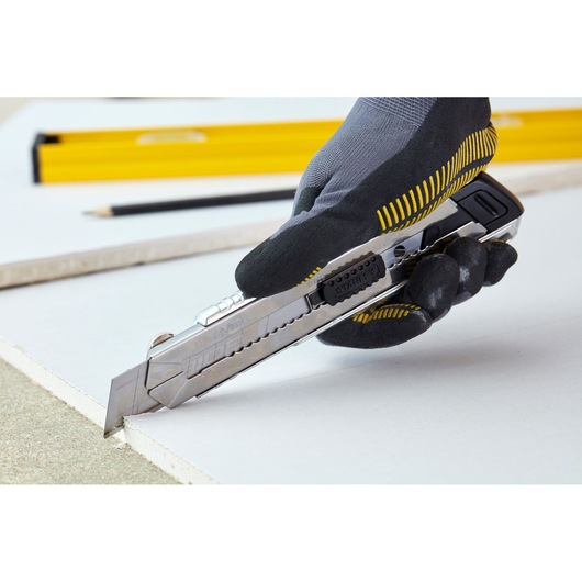 Cutter utilitaire STANLEY 0-10-820 découpant du placoplâtre, tenu par une main gantée, vue latérale.