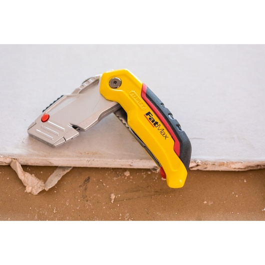 STANLEY 0-10-825 couteau utilitaire FatMax sur plaque de plâtre, poignée ergonomique jaune et noire.