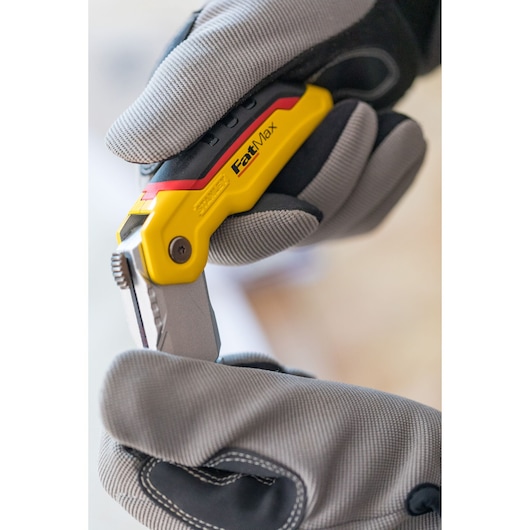 Photo du couteau utilitaire pliant STANLEY 0-10-825 tenu avec des gants, manche jaune et noir visible.