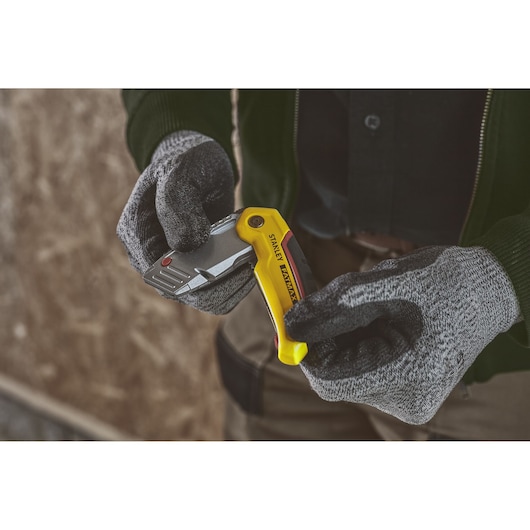 Photo du couteau utilitaire pliant STANLEY 0-10-825 à manche jaune tenu par des mains gantées, intérieur.