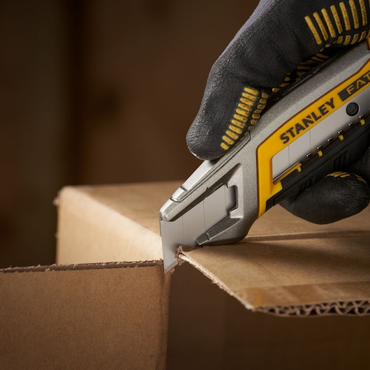 Foto van STANLEY 0-11-301 hobbymes dat karton snijdt, close-up met gehandschoende hand.