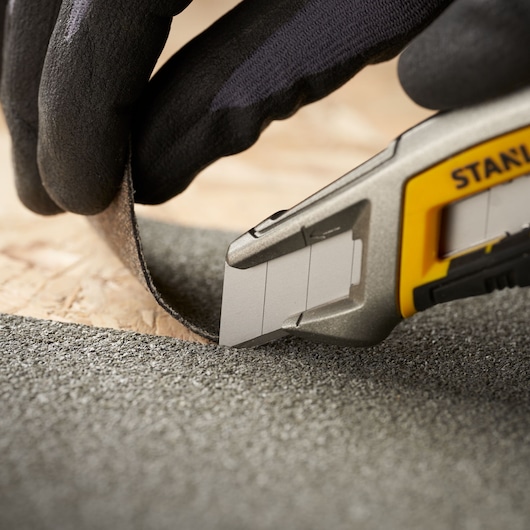 Foto van STANLEY 0-11-301 afbreekmes die schuurmateriaal snijdt, close-up, gehandschoende hand houdt materiaal.