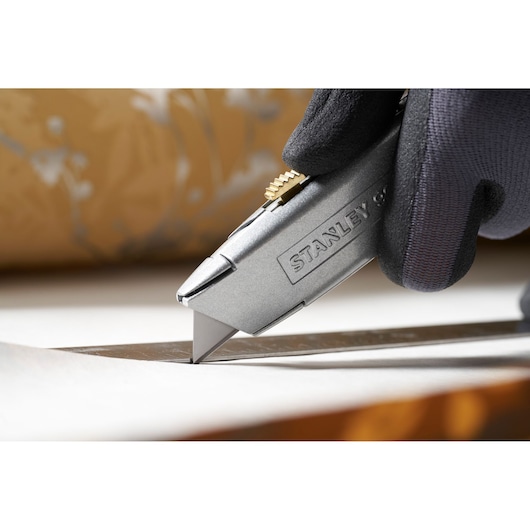 Photo du couteau utilitaire STANLEY 0-11-911 découpant du papier, tenu par une main gantée.