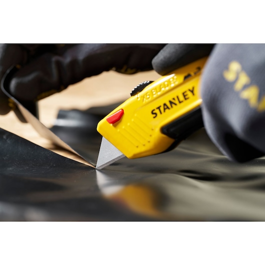 STANLEY 0-11-921 breekmes met gele handgreep snijdt zwart materiaal, close-up tijdens gebruik.