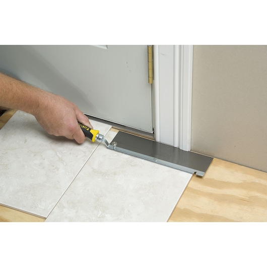 Scie pour sol STANLEY 0-15-252 coupant sous un cadre de porte, vue en angle droit.