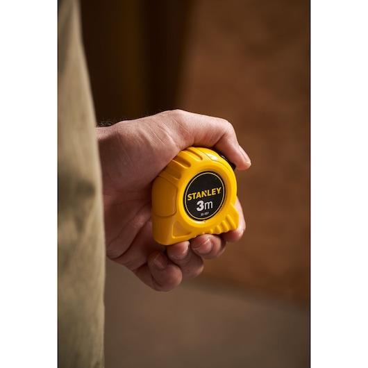 Foto van de gele STANLEY 0-30-487 rolmaat, 3 meter, compact ontwerp, vastgehouden in een hand.
