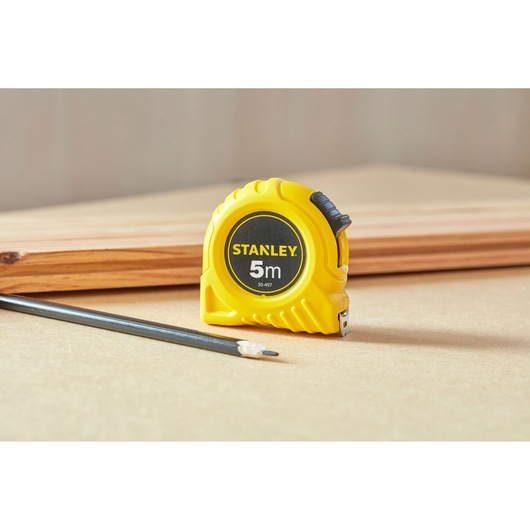 STANLEY 0-30-497 gele 5m rolbandmaat op werkbank met potlood en hout op de achtergrond.