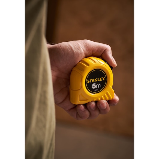 Foto van STANLEY 0-30-497 gele 5m rolmaat vastgehouden in een hand, productcategorie fotografie.