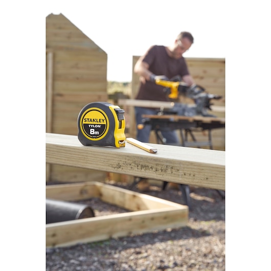 STANLEY 0-30-657 rolmaat met geel-zwart omhulsel, 8m, op hout bij bouwlocatie.