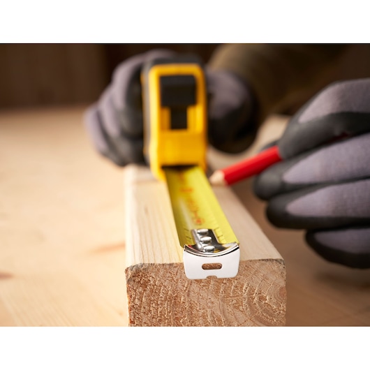 Foto van STANLEY 0-30-657 rolmaat op hout uitgelegd, persoon markeert met potlood, close-up.