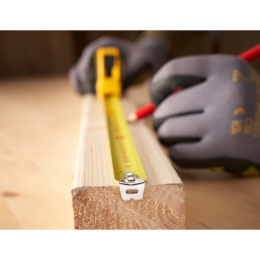 Foto van STANLEY 0-30-697 rolmaat uitgestrekt op hout met een gehandschoende hand die een maat markeert.