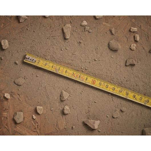 Stanley 0-32-125 gele meetlint op stoffige grond met verspreide stenen, plat gefotografeerd.