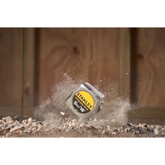 STANLEY 0-33-158 PowerLock rolmaat op rotsachtige grond met bewegende stof, productfotografie.