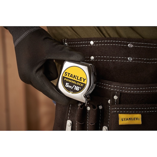 STANLEY 0-33-158 rolmaat vastgehouden door een handschoen, aan een bruine gereedschapsriem geklipt.