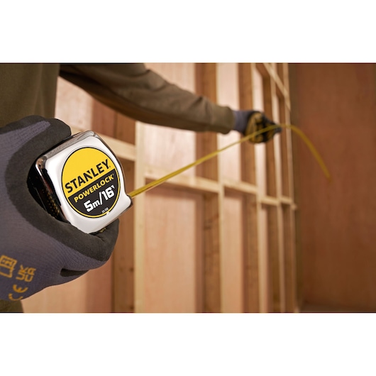 STANLEY 0-33-158 PowerLock rolmaat vastgehouden door een gehandschoende hand, meet houten wandframe.