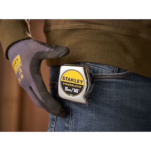STANLEY 0-33-158 PowerLock rolmaat aan een spijkerbroekzak geklemd, close-up van een gehandschoende hand.