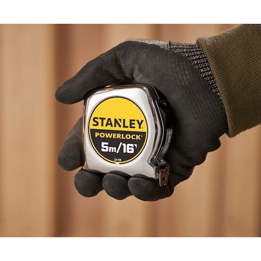 Foto van STANLEY 0-33-158 PowerLock rolmaat vastgehouden in een gehandschoende hand, 5m/16ft zichtbaar.