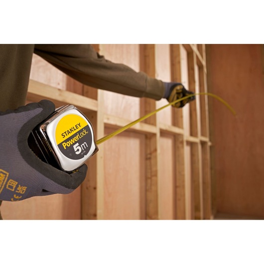 STANLEY 0-33-195 PowerLock 5m rolmaat in gehandschoende hand, meten van houten wandframe.