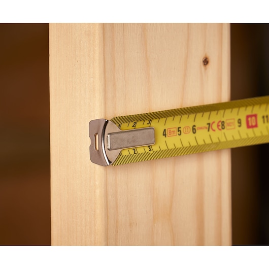 Stanley 0-33-527 rolmaat met gele band en metalen haak meet houten plank, close-up.