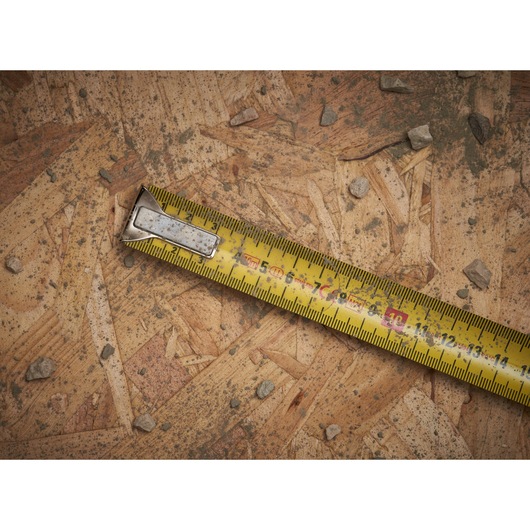STANLEY 0-33-532 gele rolmaat op houten plaat met verspreide stenen, close-up.