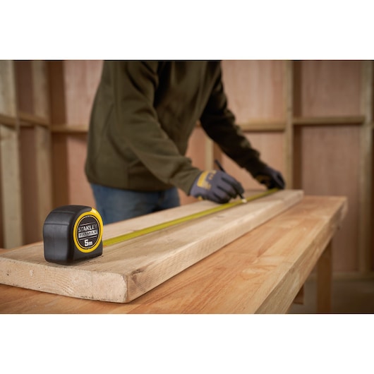 STANLEY 0-33-720 rolmaat op houten plank, persoon markeert maat in werkplaats.