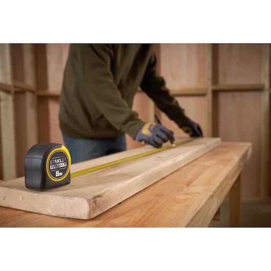 STANLEY 0-33-728 rolmaat, geel en zwart, op houten plank tijdens houtbewerking, close-up.