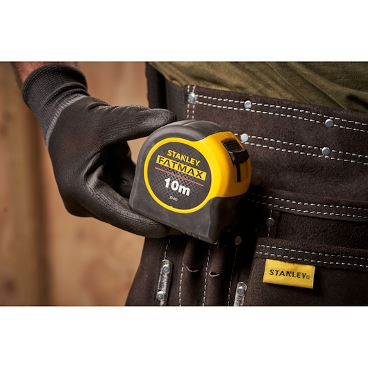 STANLEY 0-33-811 FATMAX 10m rolmaat in gehandschoende hand, vastgemaakt aan gereedschapsriem, close-up.