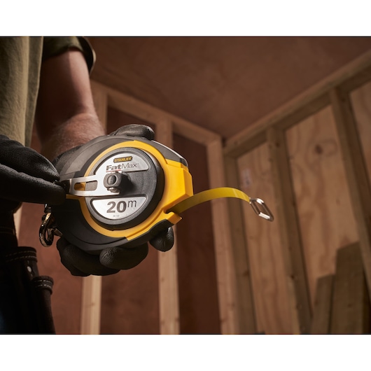 Foto van STANLEY 0-34-133 FatMax 20m meetlint vastgehouden door een gehandschoende hand op bouwlocatie.