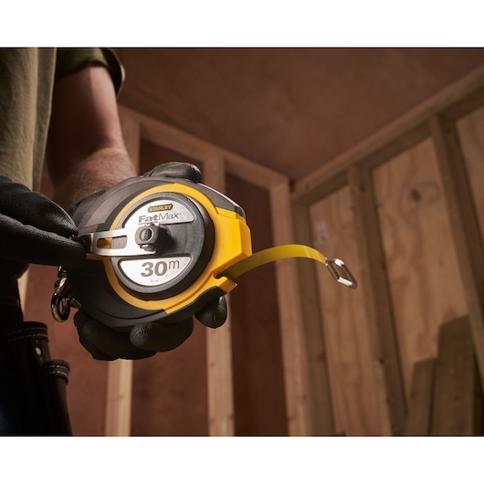 STANLEY 0-34-134 FatMax 30m meetlint vastgehouden in een gehandschoende hand op een bouwplaats.