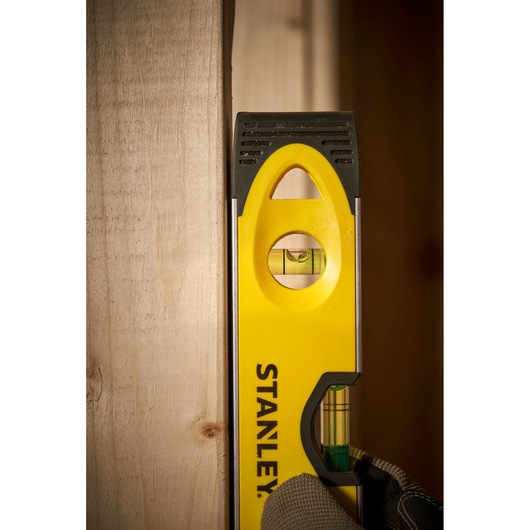 Foto van STANLEY 0-43-511 waterpas, verticaal tegen hout gehouden, zichtbare fles en gele behuizing.