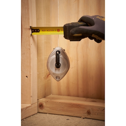 STANLEY 0-47-100 krijtlijn gereedschap in gebruik, verticaal hangend met hand die afstand meet, bouwomgeving.