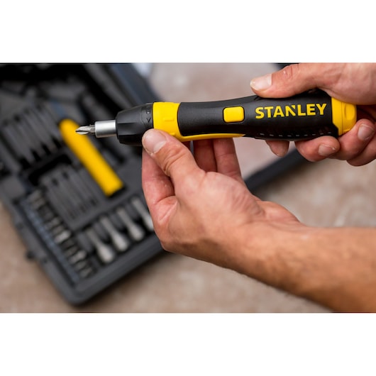 STANLEY 0-63-038 ratelende schroevendraaier met zwart-geel handvat in hand, gereedschapskist op de achtergrond.