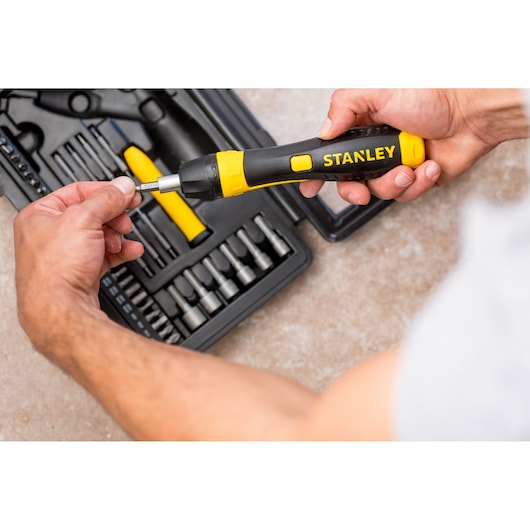 STANLEY 0-63-038 ratelschroevendraaierset met zwart-gele handgreep, persoon plaatst bit, bovenaanzicht.