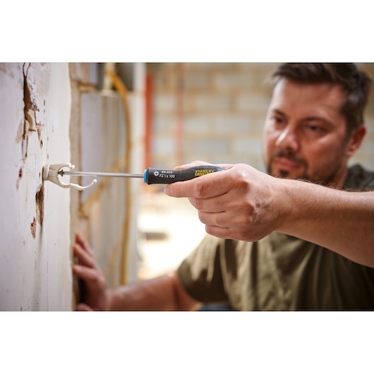Stanley 0-65-335 tournevis en utilisation, gros plan sur une main installant un support mural, chantier.