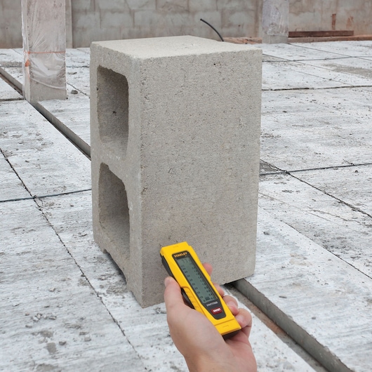 STANLEY 0-77-030 télémètre laser à boîtier jaune tenu près d’un parpaing sur chantier.