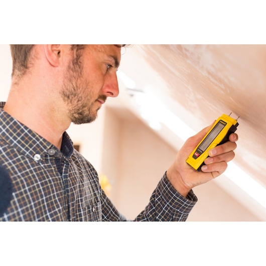 STANLEY 0-77-030 humidimètre utilisé contre un mur, outil manuel jaune, produit en utilisation.