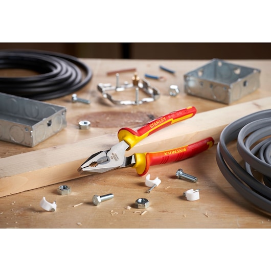 Foto van STANLEY 0-84-001 geïsoleerde combinatietang met rood-gele handgrepen op werkbank met elektrische onderdelen.