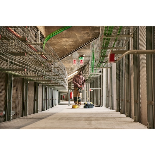 STANLEY 0-84-004 elektricien werkt met gereedschap in een grote industriële ruimte, gezien vanuit laag perspectief.